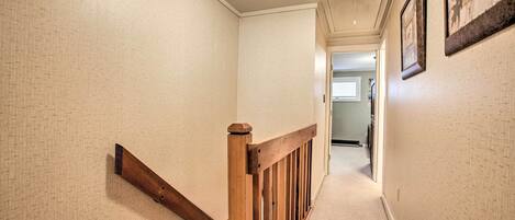 A hallway with beige textured walls, a wooden railing, and framed pictures on the wall.