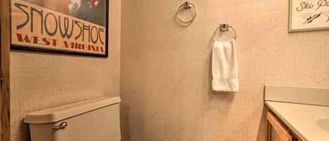 A bathroom with a toilet, a towel ring, and a framed sign on the wall.