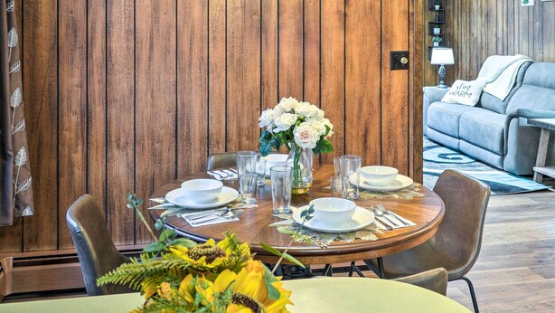 A dining area with a wooden wall, a round table set for four, and a sofa in the background.
