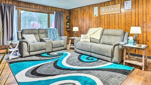 A cozy living room with two grey sofas, a patterned rug, wooden walls, and a 'Relax' sign.
