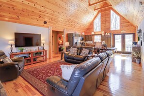 A spacious living room with a large flat-screen TV, leather sofas, and a wooden ceiling. - Deck, Gas Grill + Mtn Views: Sparta Cabin Stay! (Sparta)