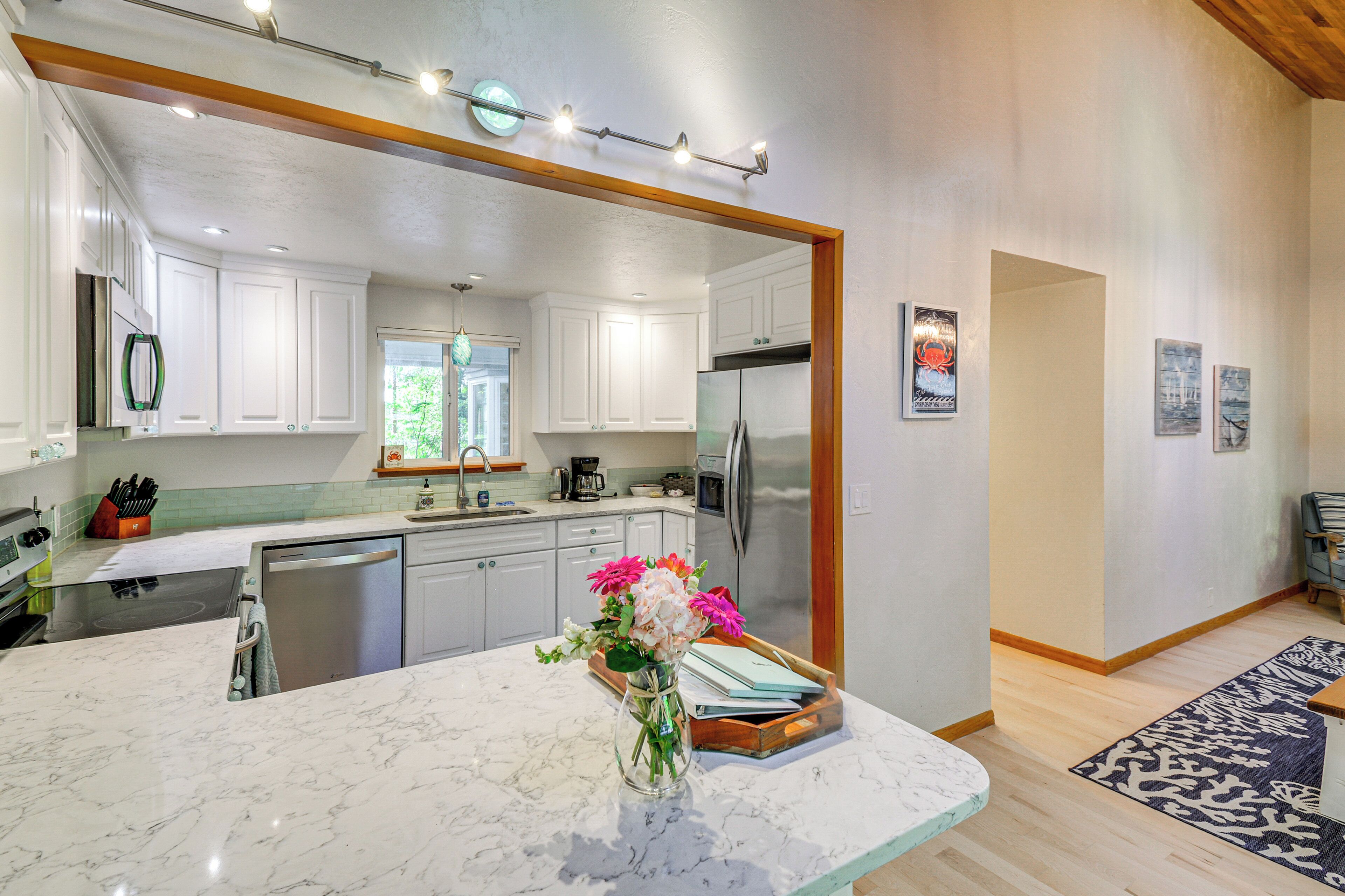 A modern kitchen with white cabinets, a stainless steel refrigerator, and a marble countertop.