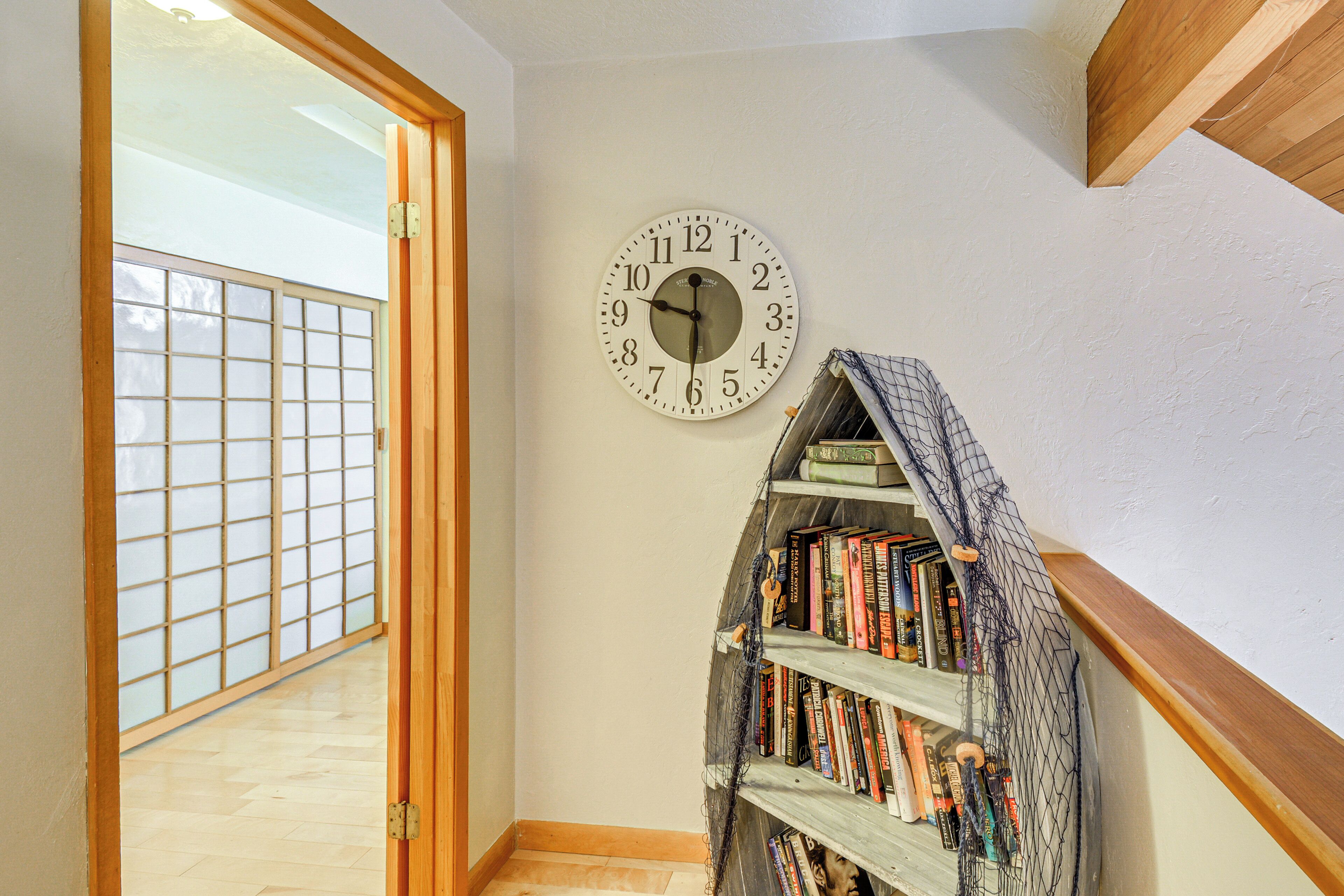 A room with a wooden bookshelf, a clock, and a sliding door leading to a balcony.