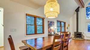 A dining area with a wooden table and chairs, large windows with blinds, a hanging light fixture, and a wood-burning stove. - Peaceful Russellville Cabin Close to Lakes! (Russellville)