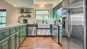 A kitchen with green cabinets, a stainless steel refrigerator, a window, and a coffee machine. - Peaceful Russellville Cabin Close to Lakes! (Russellville)