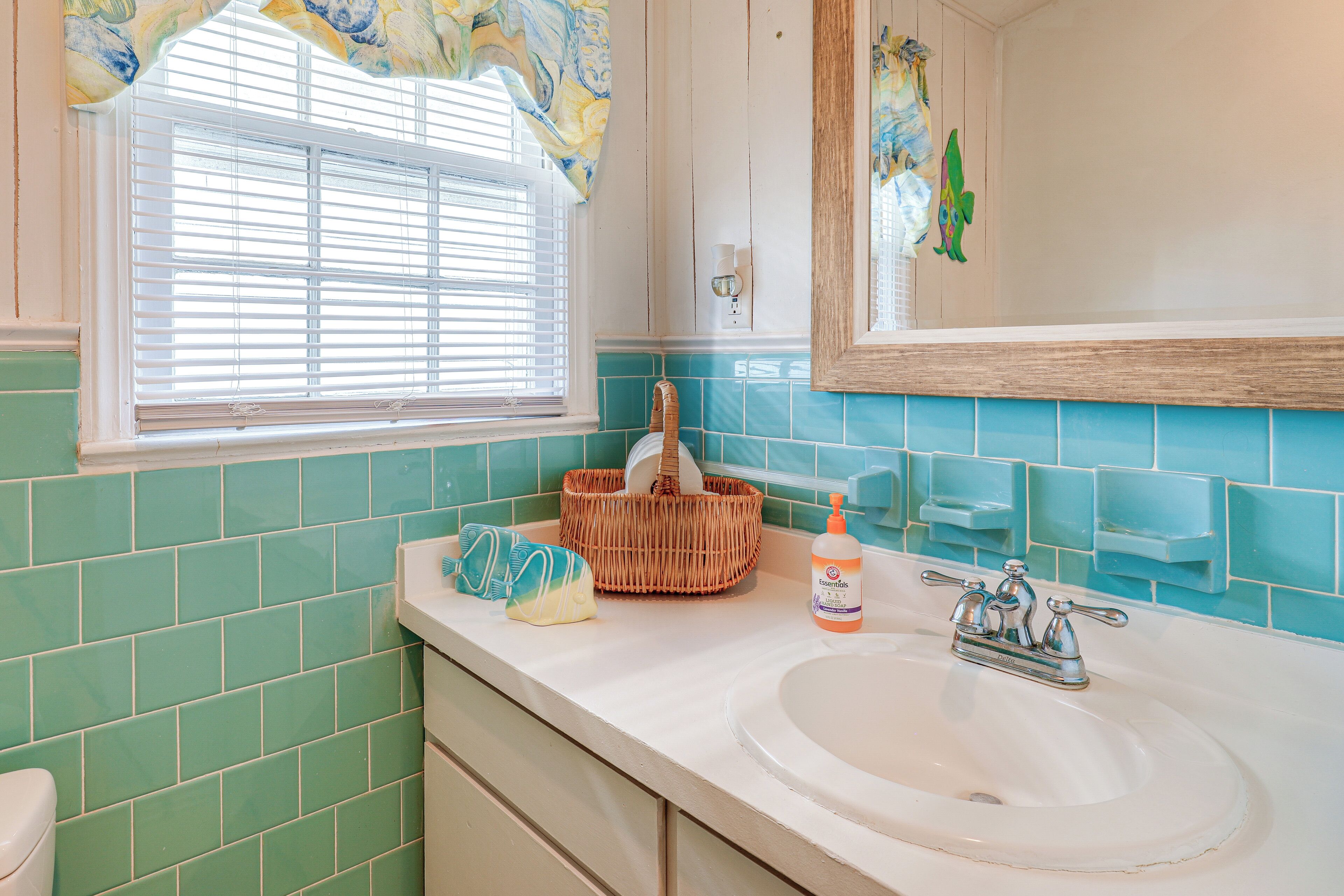 A bathroom with a white sink, a window with blinds, a mirror, and a green tiled wall.