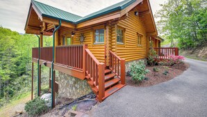 A log cabin with a stone foundation, wooden deck, and a stone wall.