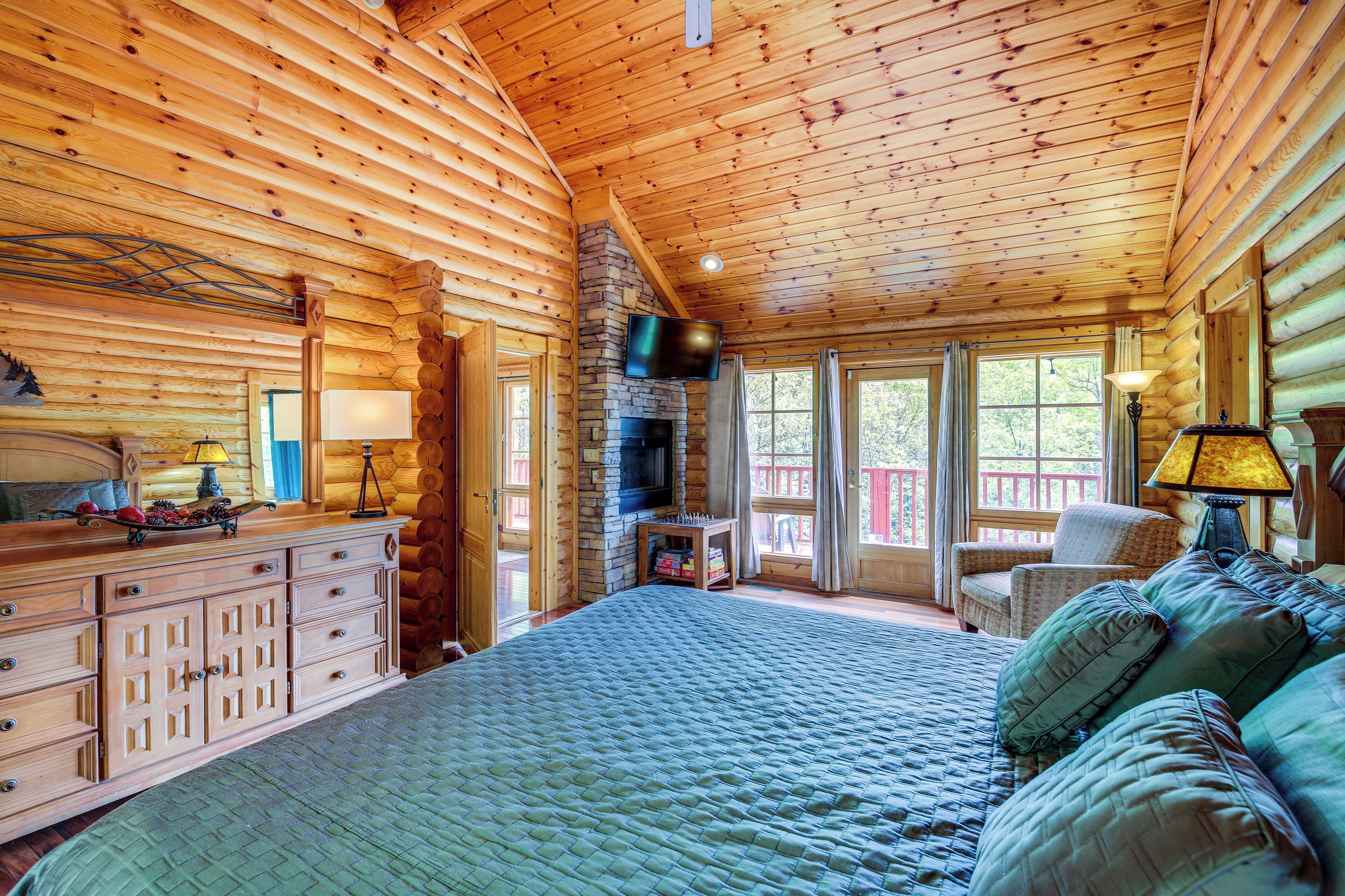 Interior de una cabaña de troncos con una cama grande, tocador de madera, chimenea de piedra y televisor montado en la pared.