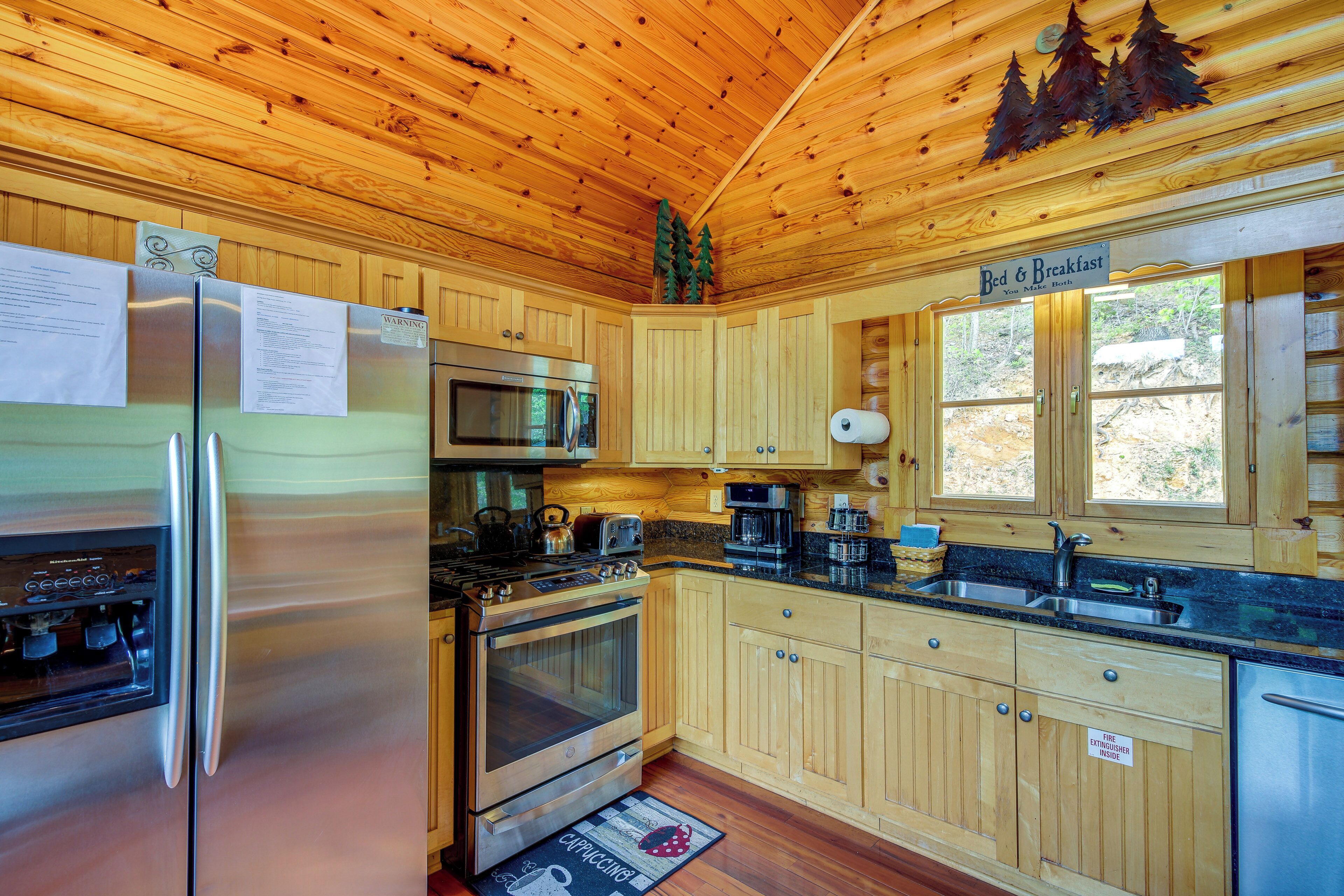 A cabin-style kitchen with wooden cabinets, a stainless steel refrigerator, a microwave, an oven, and a sink.
