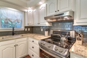A modern kitchen with white cabinetry, a stainless steel stove, and a granite countertop.