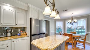 A kitchen with white cabinetry, a granite countertop, stainless steel appliances, and a dining area with wooden furniture. - Peaceful Fairhope Cottage w/ Covered Patio! (Fairhope)