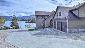 A modern two-story house with a garage, a driveway, and a lake view. - Lakefront Adirondacks Home: Fish, Hike, Ski! (Bolton Landing)