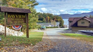 A marina sign with "Bayview Marina & Suites" and a view of boats on a lake with mountains in the background. - Lakefront Adirondacks Home: Fish, Hike, Ski! (Bolton Landing)
