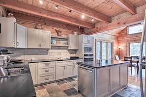 A modern kitchen with white cabinets, a black countertop, and a built-in dishwasher. There are multiple windows providing natural light and a view of the outdoors. - Thunder Lake Escape + Boat Dock! (Remer)