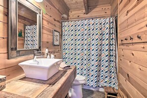 A wooden cabin bathroom with a white sink, a mirror, a toilet, and a shower curtain with a chevron pattern. - Thunder Lake Escape + Boat Dock! (Remer)