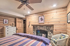 A cozy log cabin room with a bed, a fireplace, a ceiling fan, and wooden walls. - Thunder Lake Escape + Boat Dock! (Remer)