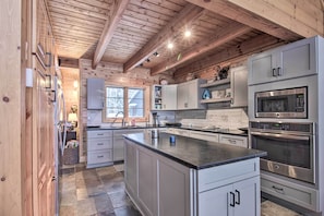 A modern kitchen with wooden ceiling beams, stainless steel appliances, and a large island. - Thunder Lake Escape + Boat Dock! (Remer)