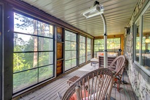 A wooden deck with large windows, wicker chairs, and a stone wall. - Thunder Lake Escape + Boat Dock! (Remer)
