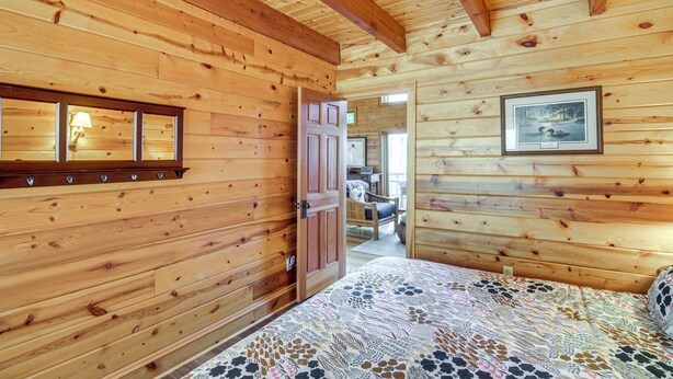 A wooden cabin interior with a bed, a door leading to a bathroom, and a framed picture on the wall. - Thunder Lake Escape + Boat Dock! (Remer)