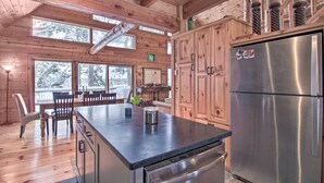A cabin-style kitchen with wooden walls, a large refrigerator, and a dining area with chairs and a table. - Thunder Lake Escape + Boat Dock! (Remer)