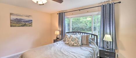 A bedroom with a bed, nightstands, a ceiling fan, a window with curtains, and a wall-mounted lamp.
