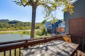 A wooden deck with a bench overlooking a lake, surrounded by trees and a view of a residential area with houses.