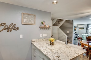 A kitchen with a marble countertop, a wall-mounted shelf with flags, and a sign that reads 'There's no place like our PLACE.'