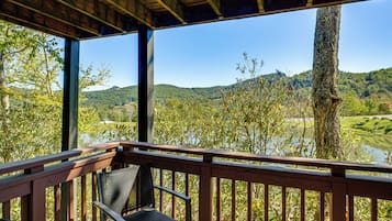 A wooden deck with a bench overlooking a river and hills.