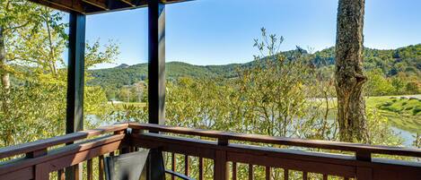 Une terrasse en bois avec un banc donnant sur une rivière et des collines.