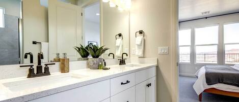 Un bagno moderno con uno specchio grande, un piano di lavoro bianco e un lavandino. Asciugamani appesi al muro e una pianta in vaso sul piano.