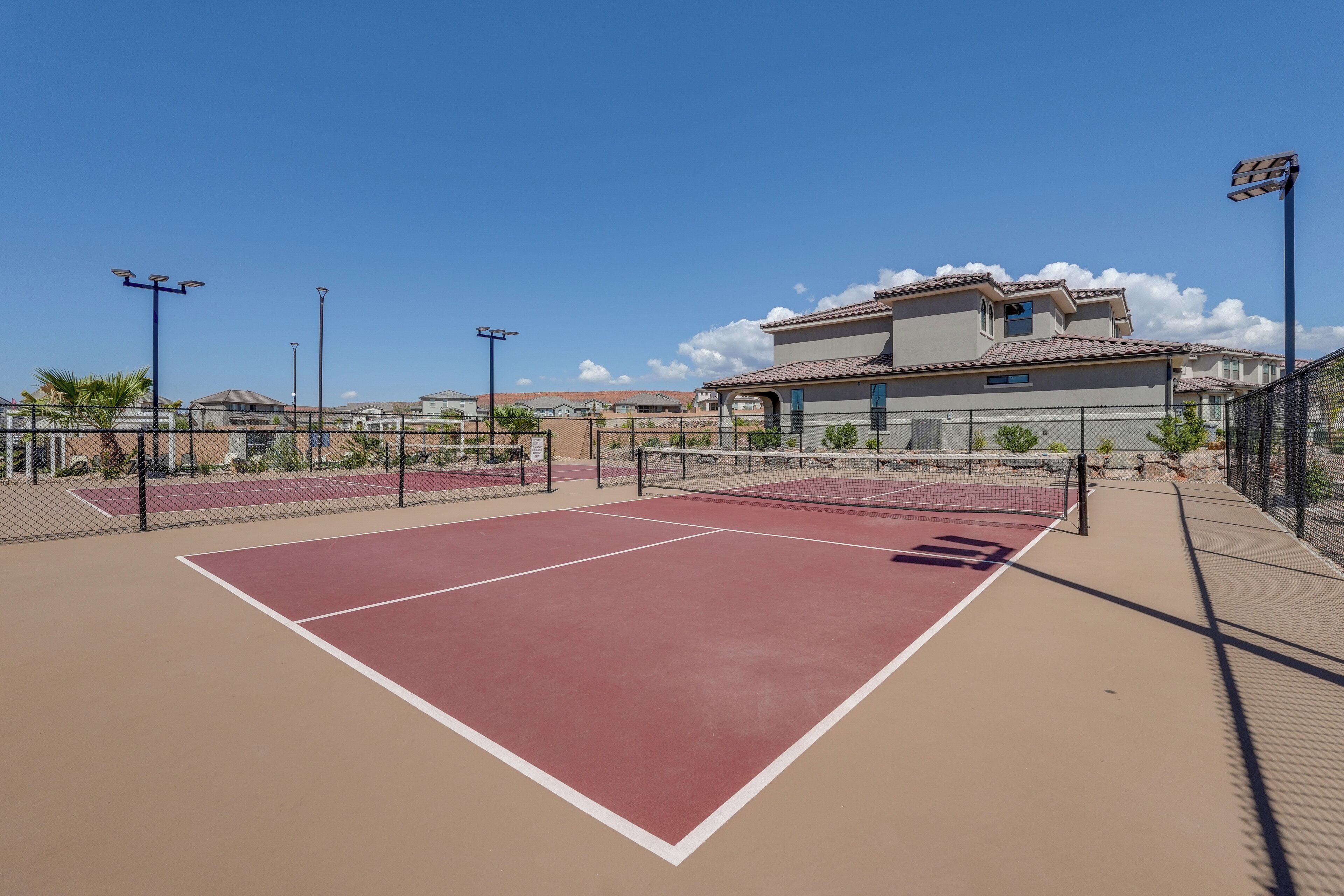 Cancha de tenis con una red, rodeada por una valla y adyacente a un edificio con tejado de tejas.