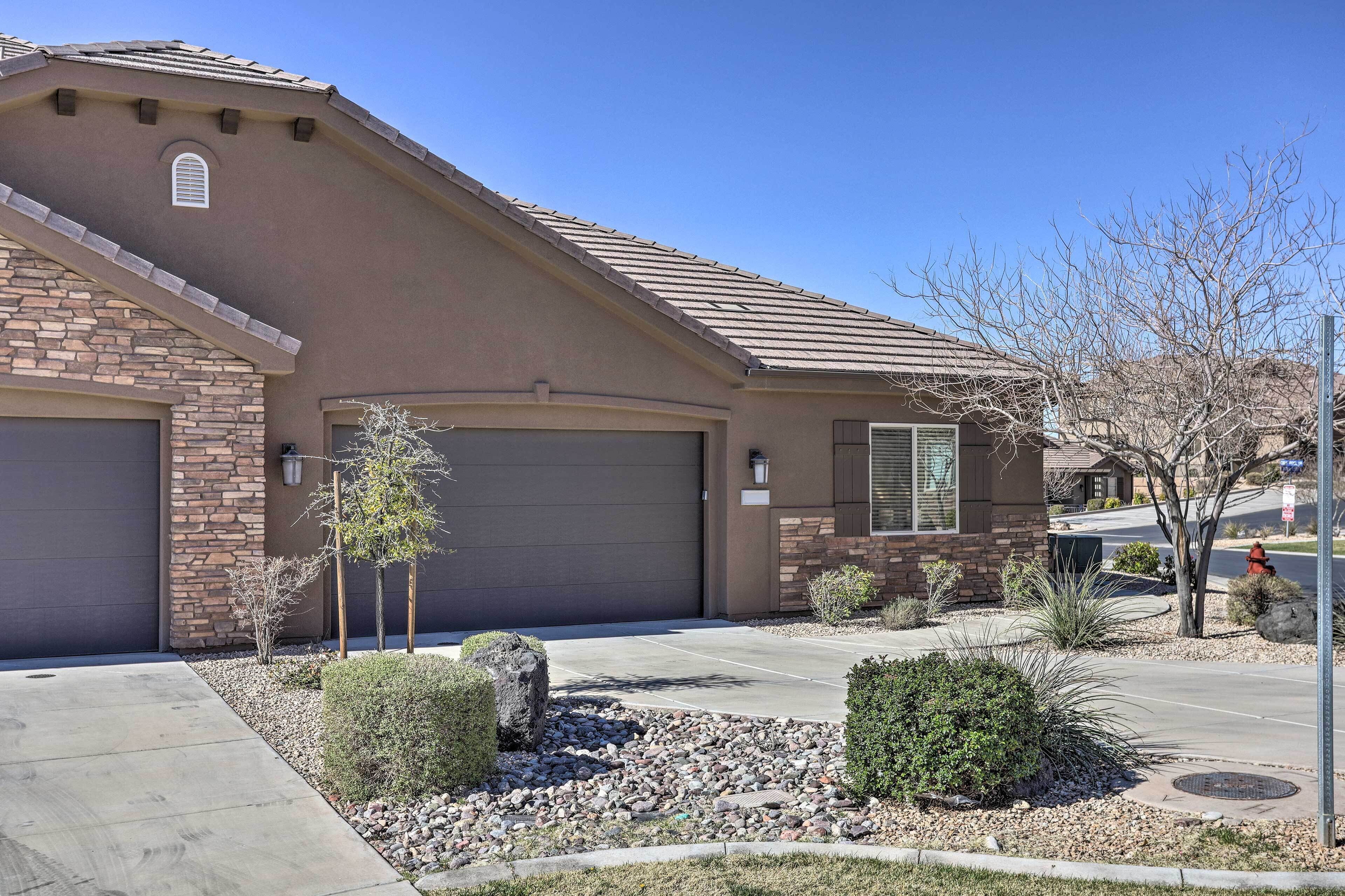 A residential house with a garage, a stone facade, and a landscaped front yard with shrubs and a small tree.