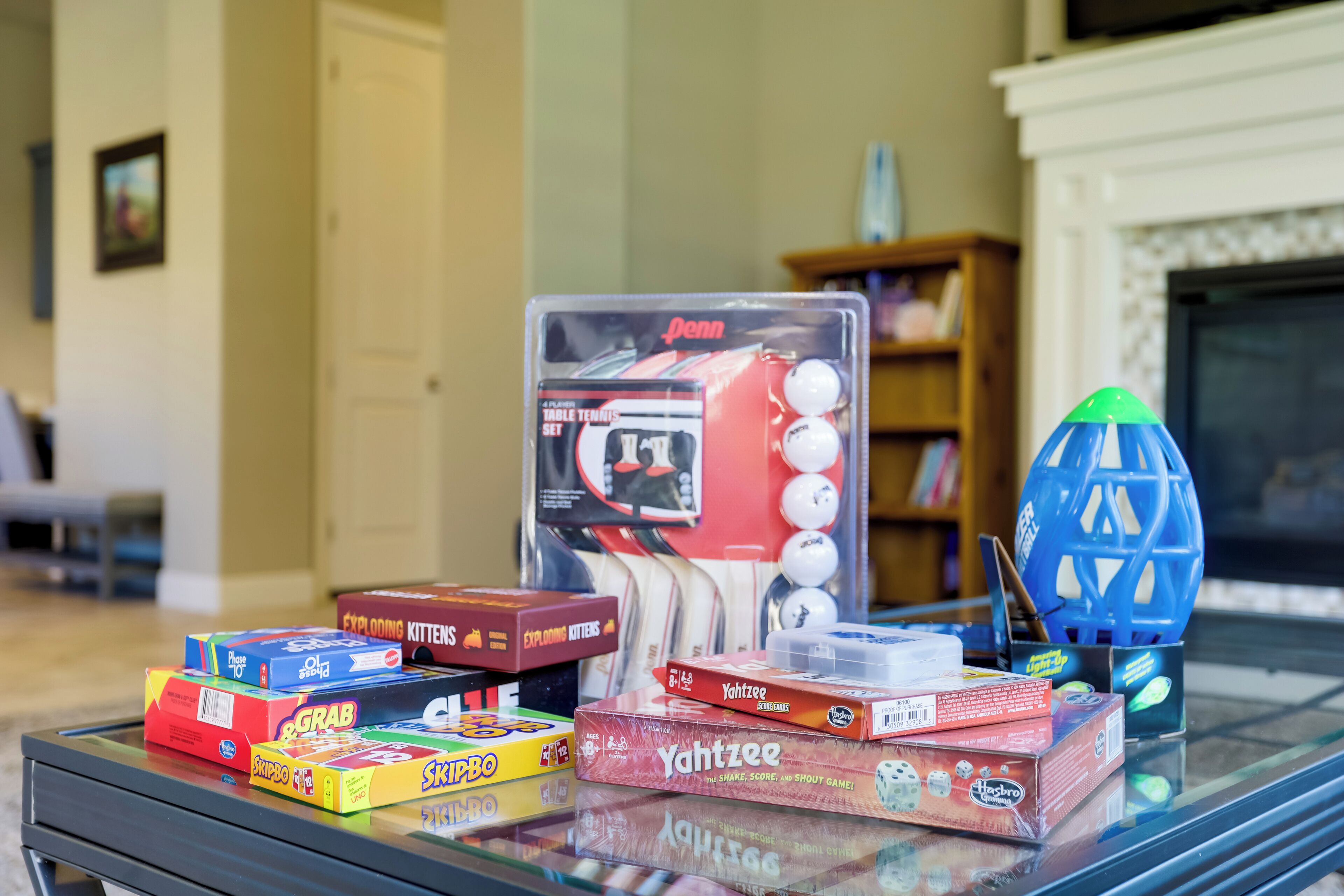 A table with various board games and a blue toy in a living room.