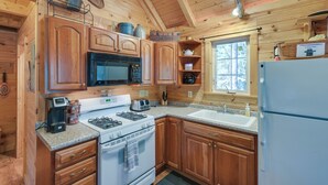 A wooden cabin kitchen with a microwave, stove, sink, and cabinets. - Maine Lodging Near Acadia National Park! (Bernard)