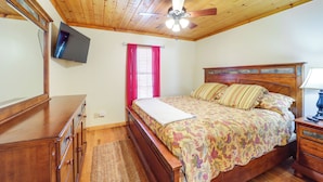 A bedroom with a wooden ceiling, a bed with floral bedding, a wooden dresser, and a television mounted on the wall. - Secluded Lenoir Cabin: 4 Mi to Dtwn Blowing Rock (Lenoir)