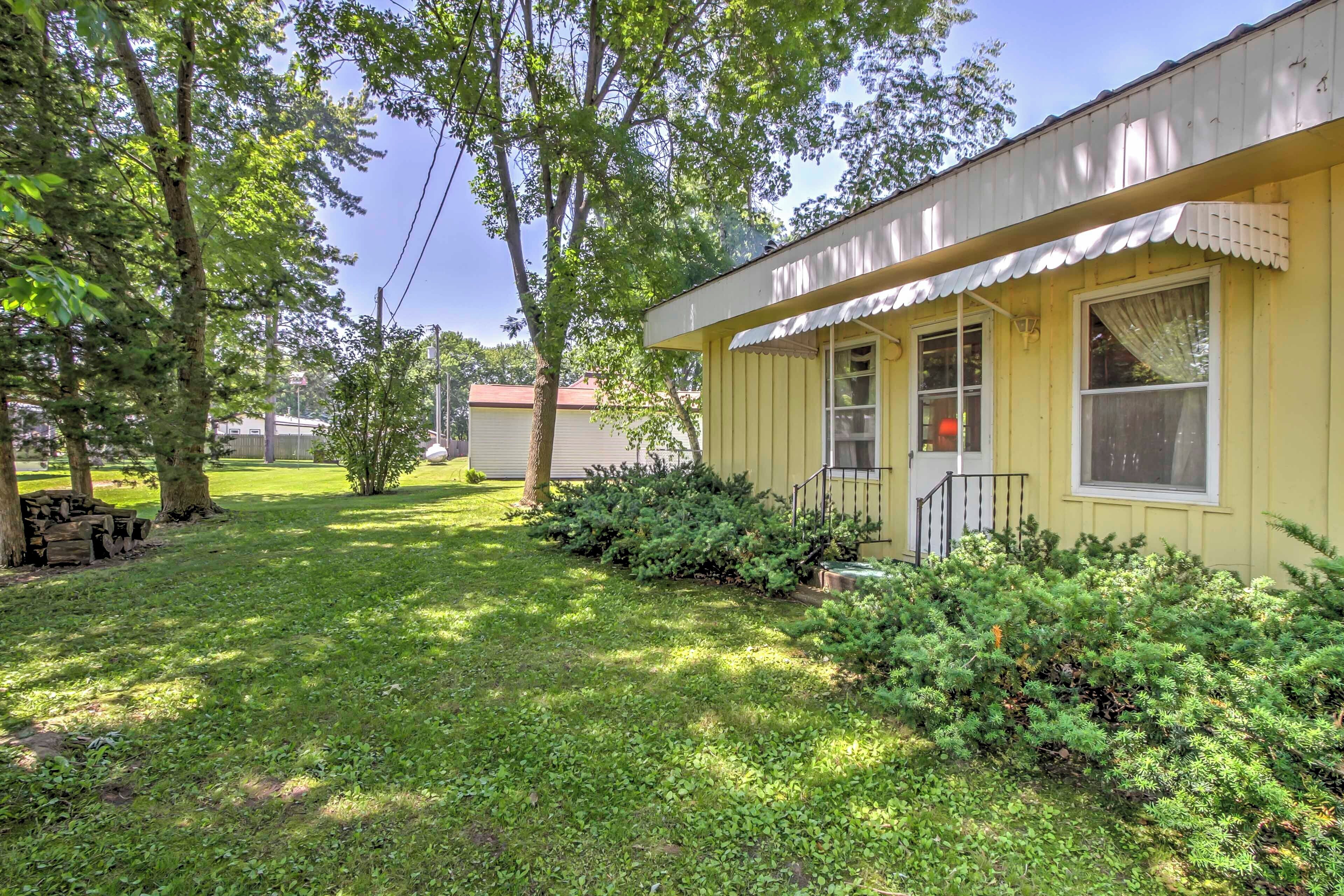 A yellow single-story house with a front porch, a small front yard with grass and shrubs, and a tree to the left.
