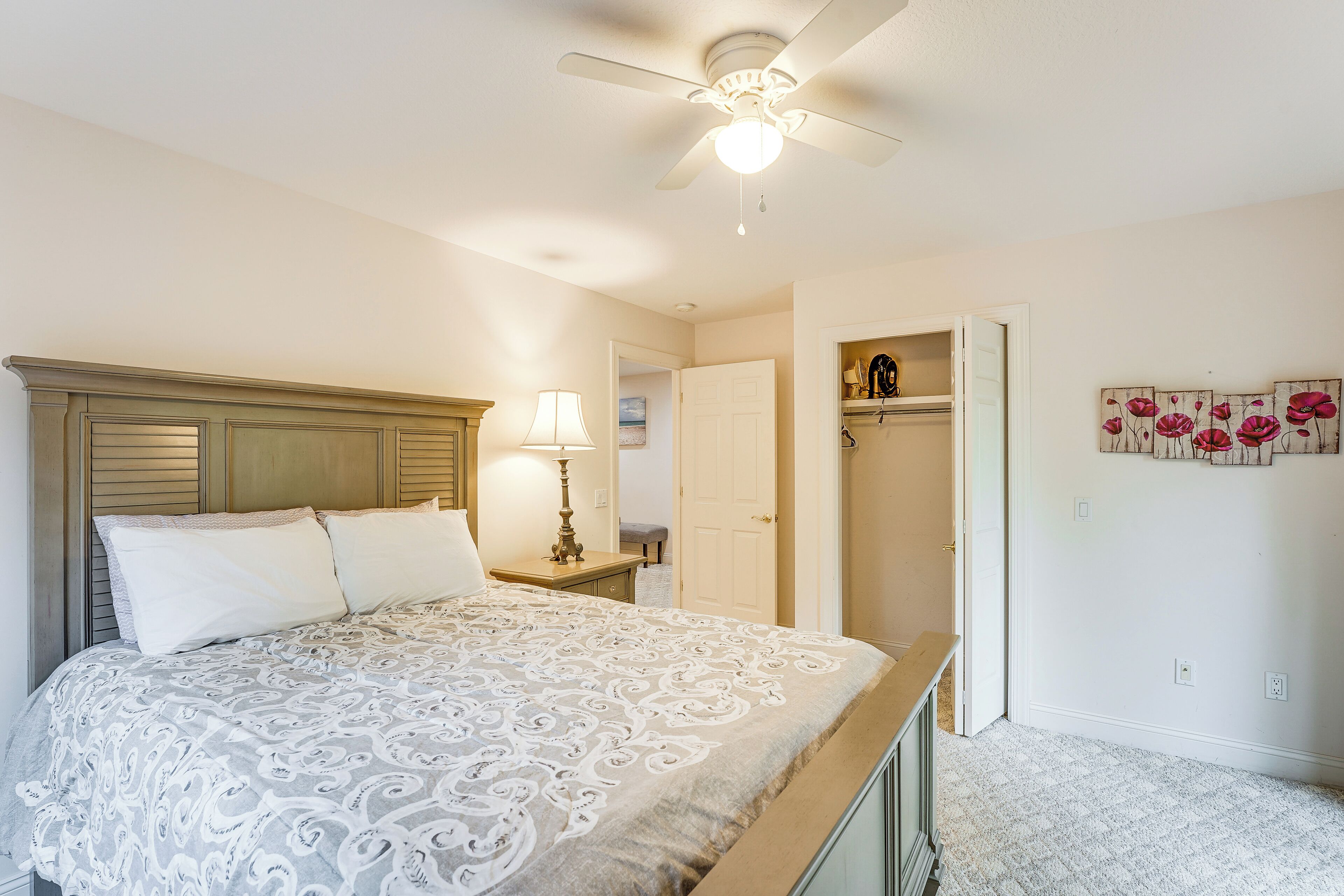 A bedroom with a bed, a ceiling fan, a nightstand, a lamp, and a door leading to another room.