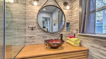 A bathroom with a wooden vanity, a round marble sink, a large mirror, and a window with a view.