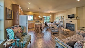 A spacious living room with a large sofa, a coffee table, and a fireplace. There is a kitchen area with wooden cabinets and a dining table. - Unique Townhouse in Bavarian-style Neighborhood! (Adamstown)