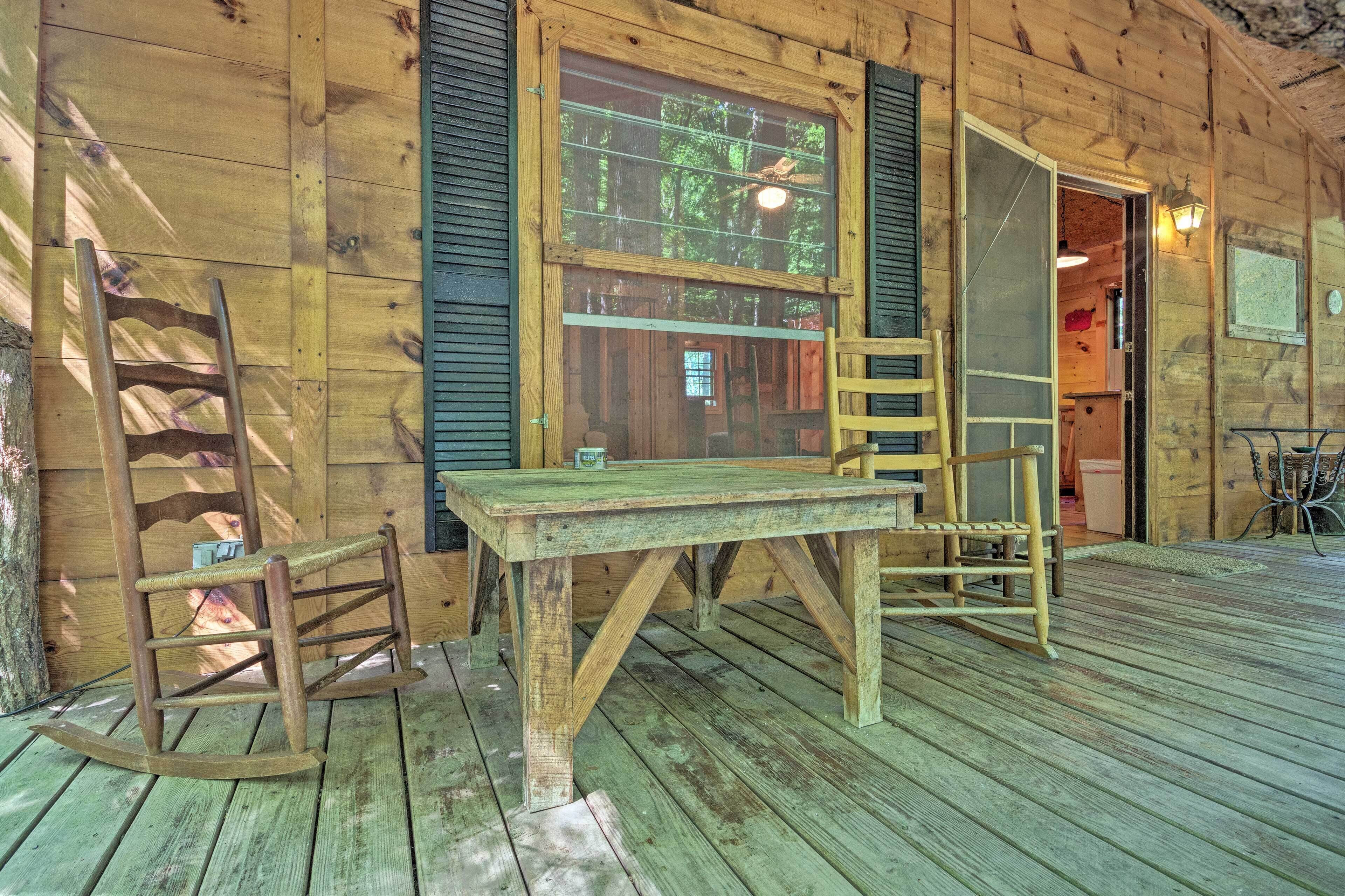 A wooden cabin with a wooden table and two rocking chairs on a porch.