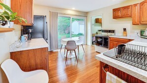Una cocina moderna con armarios de madera, un comedor con mesa y sillas blancas, y un amplio ventanal con vistas al exterior.