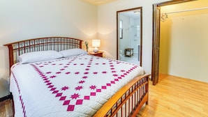 Una cama bien tendida con un edredón blanco y rosa, un cabecero de madera y una mesita de noche con una lámpara.
