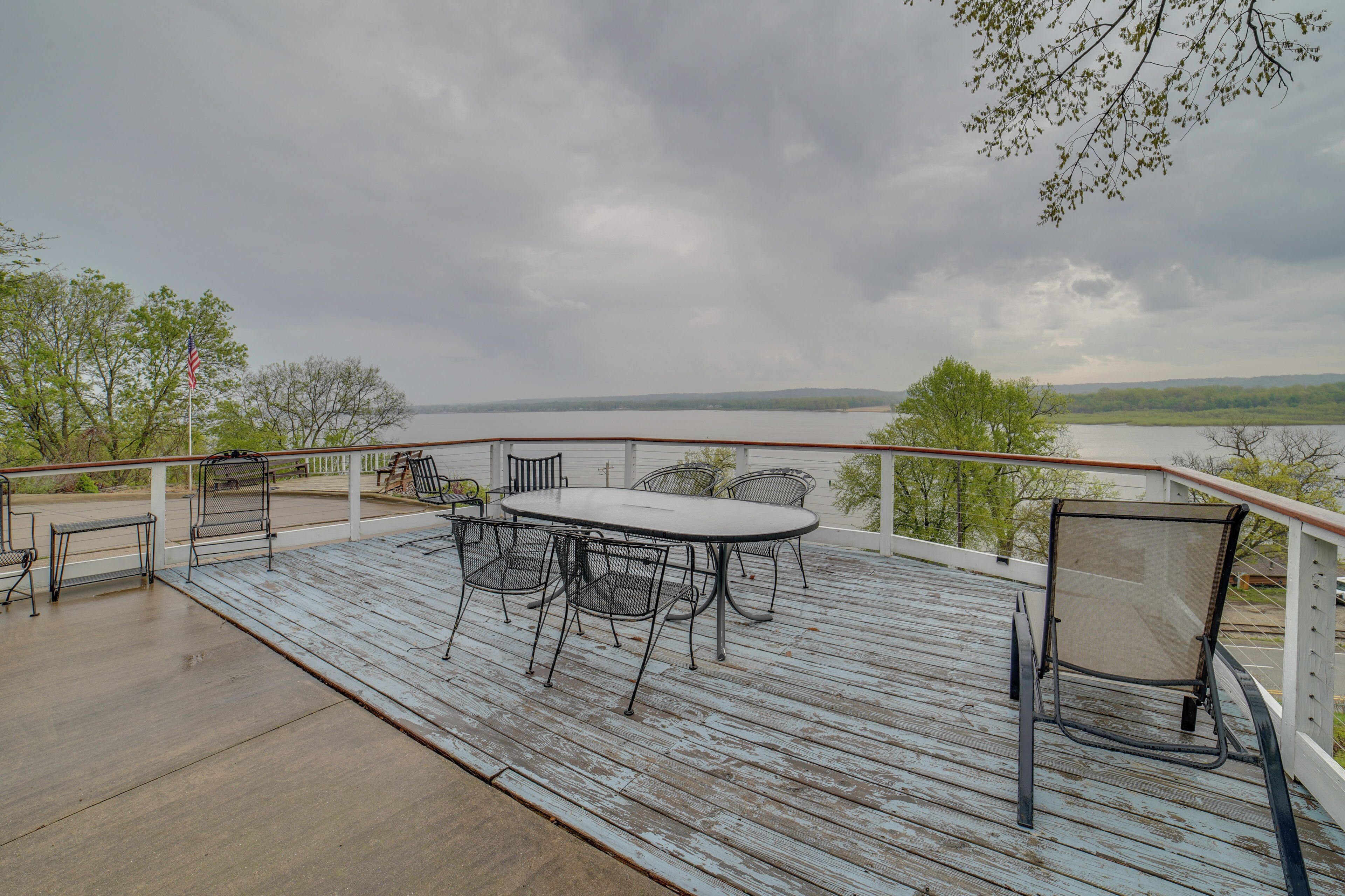 A wooden deck with a table and chairs, overlooking a body of water and trees.