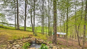 A rustic outdoor setting with a stone pond, a wooden structure, and a grassy area surrounded by trees. - Wellington Cabin Escape w/ Wraparound Deck! (Wellington)