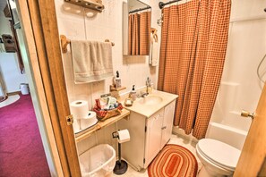 A bathroom with a white sink, mirror, and toilet. There is a red and white checkered shower curtain, a white towel hanging on a rack, and a red and white patterned rug on the floor.