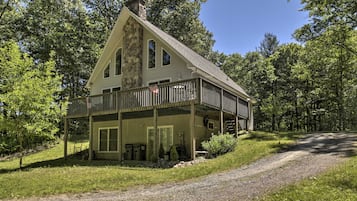 A two-story house with a stone chimney, a balcony, and a gravel driveway.