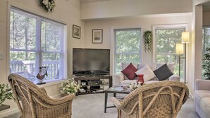 A living room with a flat-screen TV, wicker chairs, a sofa with cushions, and large windows with blinds. - Spacious Home w/ Deck, Grill & Delaware River View (Callicoon)