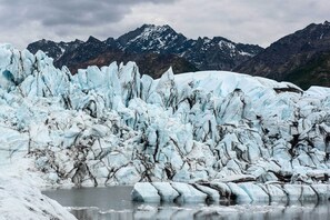 A glacier with jagged ice formations and a body of water in the foreground, with mountains in the background. - Spacious & Private Home w/ Lazy Mountain View (Palmer)