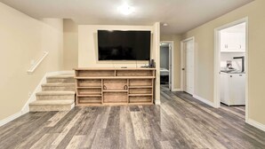 A living room with a flat-screen TV mounted on a wooden entertainment unit, carpeted stairs, and hardwood flooring. - Spacious & Private Home w/ Lazy Mountain View (Palmer)