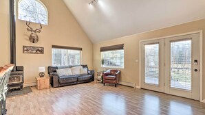 A spacious living room with a high ceiling, a fireplace, a leather sofa, and a large window with a deer head mounted on the wall. - Spacious & Private Home w/ Lazy Mountain View (Palmer)